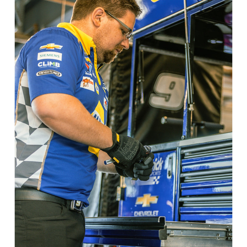 Mecánico con guantes Mechanix Wear FastFit MFF-05 negros usando una herramienta junto a un gabinete azul - DIBAMEX